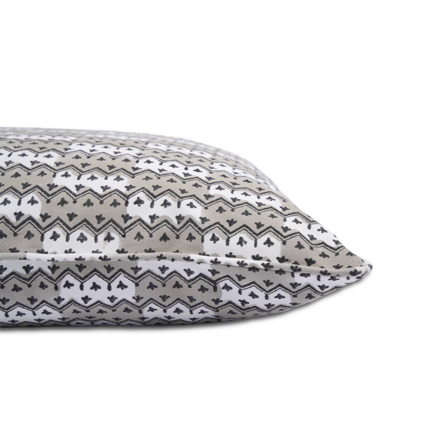 Side-profile close-up of the Munnar Stone 100% cotton block printed pillow cover resting against a clean white background. Highlights the tailored piped edge seam and the repeating soft grey, black, and white geometric chevron and botanical motif. Fine handmade artisan textile home decor.