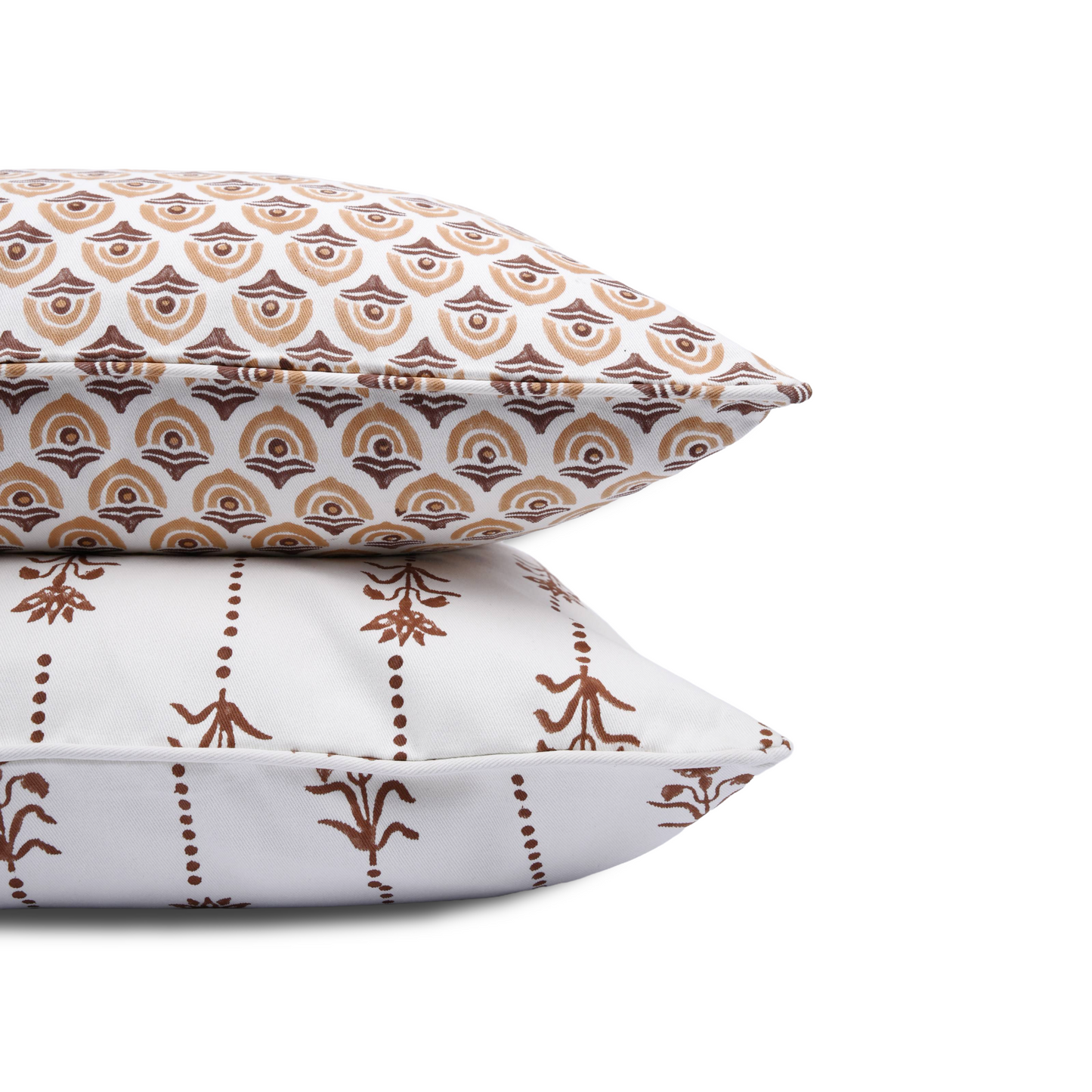 A close-up side view of two stacked 100% cotton block printed pillow covers against a clean white background. The top cushion features a repeating brown and tan scalloped geometric pattern, resting directly on the Reed Soil earthy brown floral and dotted stripe cushion cover. Highlights the tailored piped edges and crisp white fabric of these fine handmade artisan textile home decor pieces.