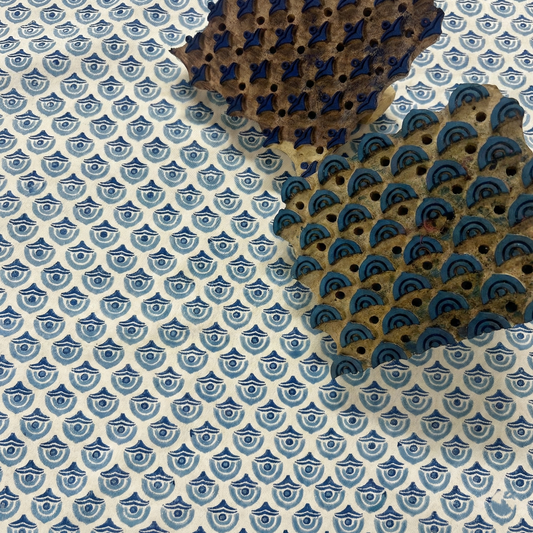 Two hand-carved wooden printing blocks resting on 100% cotton fabric featuring the Arko Cerulean scalloped arch pattern in shades of blue and navy. Behind-the-scenes detail showing the traditional hand block printing artisan process used to craft throw pillow and cushion covers.