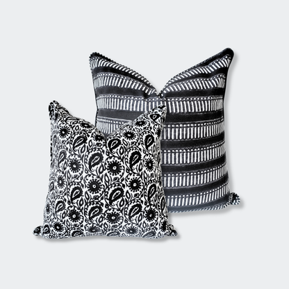 A styled duo of Homeway Living 100% cotton monochrome block-printed cushion covers. The front 18x18 pillow features the Siona Charcoal black and white floral paisley print. The back 20x20 pillow highlights a bold black design with white geometric stripes. These handmade artisan pieces offer a clean, contemporary aesthetic perfect for modern rustic styling across Canada and the US.