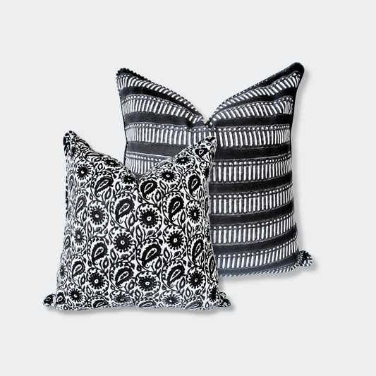A styled duo of Homeway Living 100% cotton monochrome block-printed cushion covers. The front 18x18 pillow features the Siona Charcoal black and white floral paisley print. The back 20x20 pillow highlights a bold black design with white geometric stripes. These handmade artisan pieces offer a clean, contemporary aesthetic perfect for modern rustic styling across Canada and the US.