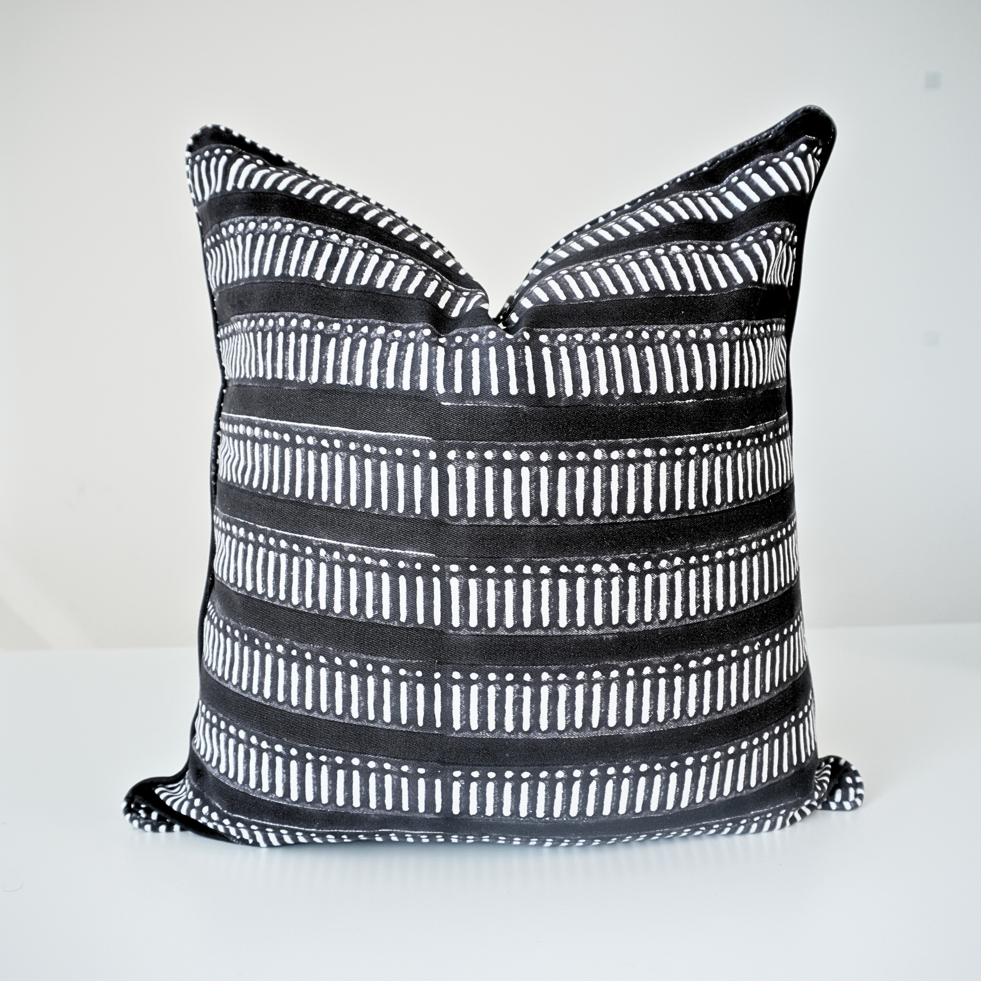 Studio product shot of a single Eko Charcoal cushion cover by Homeway Living. Handmade from 100% cotton, this block-printed pillow features a bold black base with white horizontal geometric stripes. Finished with tailored piped edges, it offers a clean, high-end aesthetic perfect for modern rustic or Scandinavian home styling in Canada and the US.