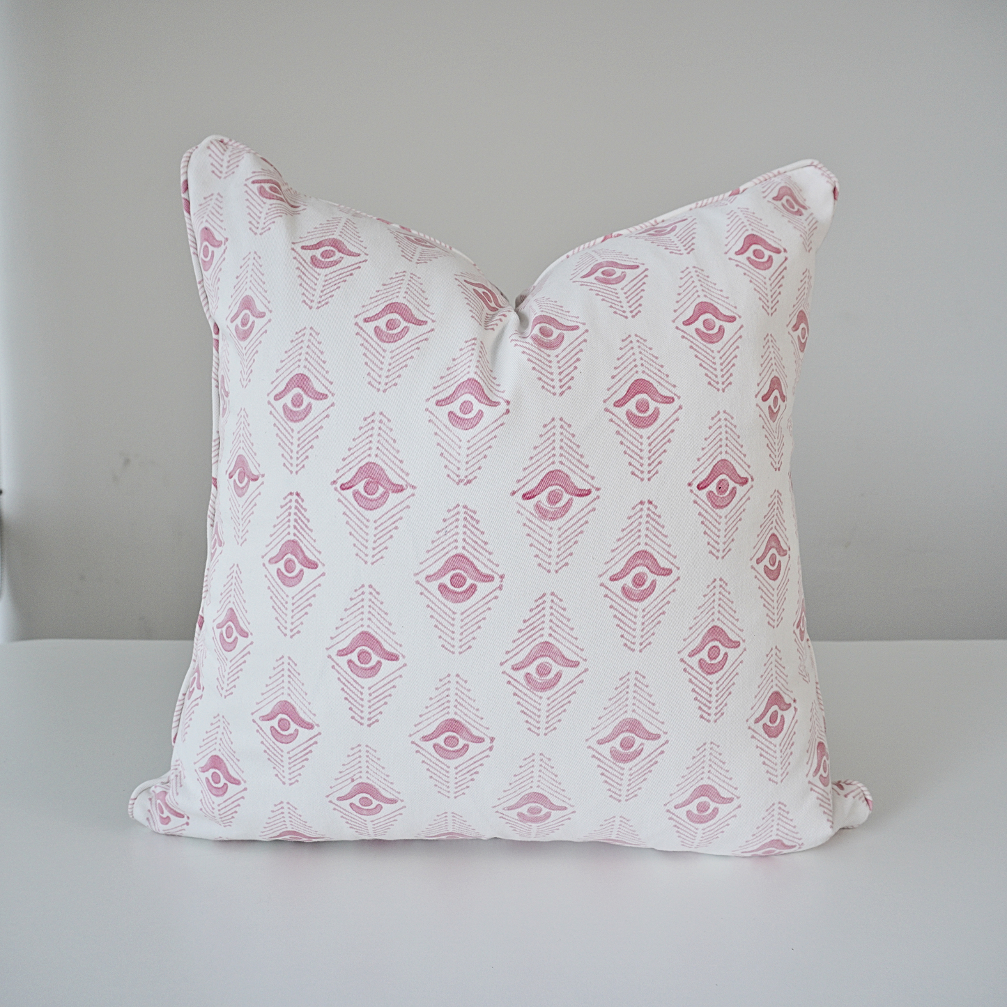 Studio product shot of a single Evia Blossom cushion cover, handcrafted from 100% cotton and centered on a white background. The design features a delicate, soft pink geometric arrow motif repeated on a crisp white base. Finished with elegant, tailored piped edges, this pillow showcases a high-end, artistic aesthetic by Homeway Living, suitable for contemporary living rooms or bedroom styling.