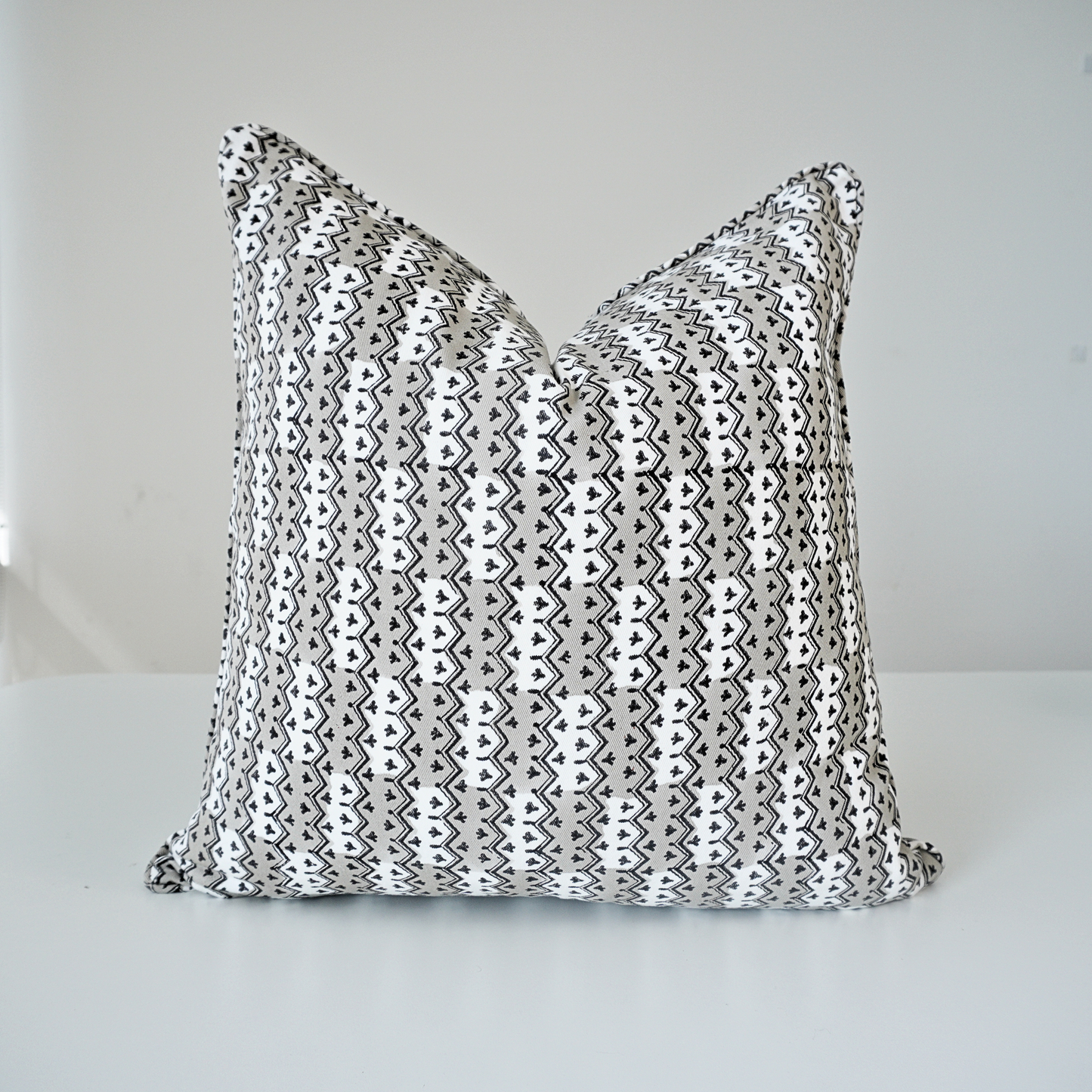 Square Munnar Stone 100% cotton block printed pillow cover. This artisan throw cushion features a repeating geometric vertical chevron and small botanical motif pattern in soft grey, black, and white. Finished with tailored piped edges against a crisp white background, showcasing fine handmade textile home decor.