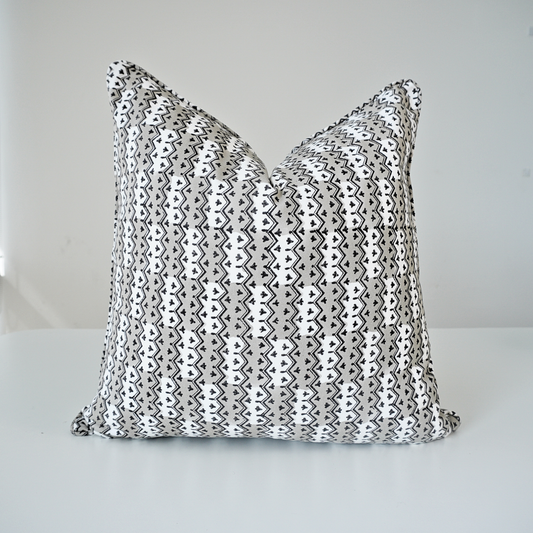 Square Munnar Stone 100% cotton block printed pillow cover. This artisan throw cushion features a repeating geometric vertical chevron and small botanical motif pattern in soft grey, black, and white. Finished with tailored piped edges against a crisp white background, showcasing fine handmade textile home decor.