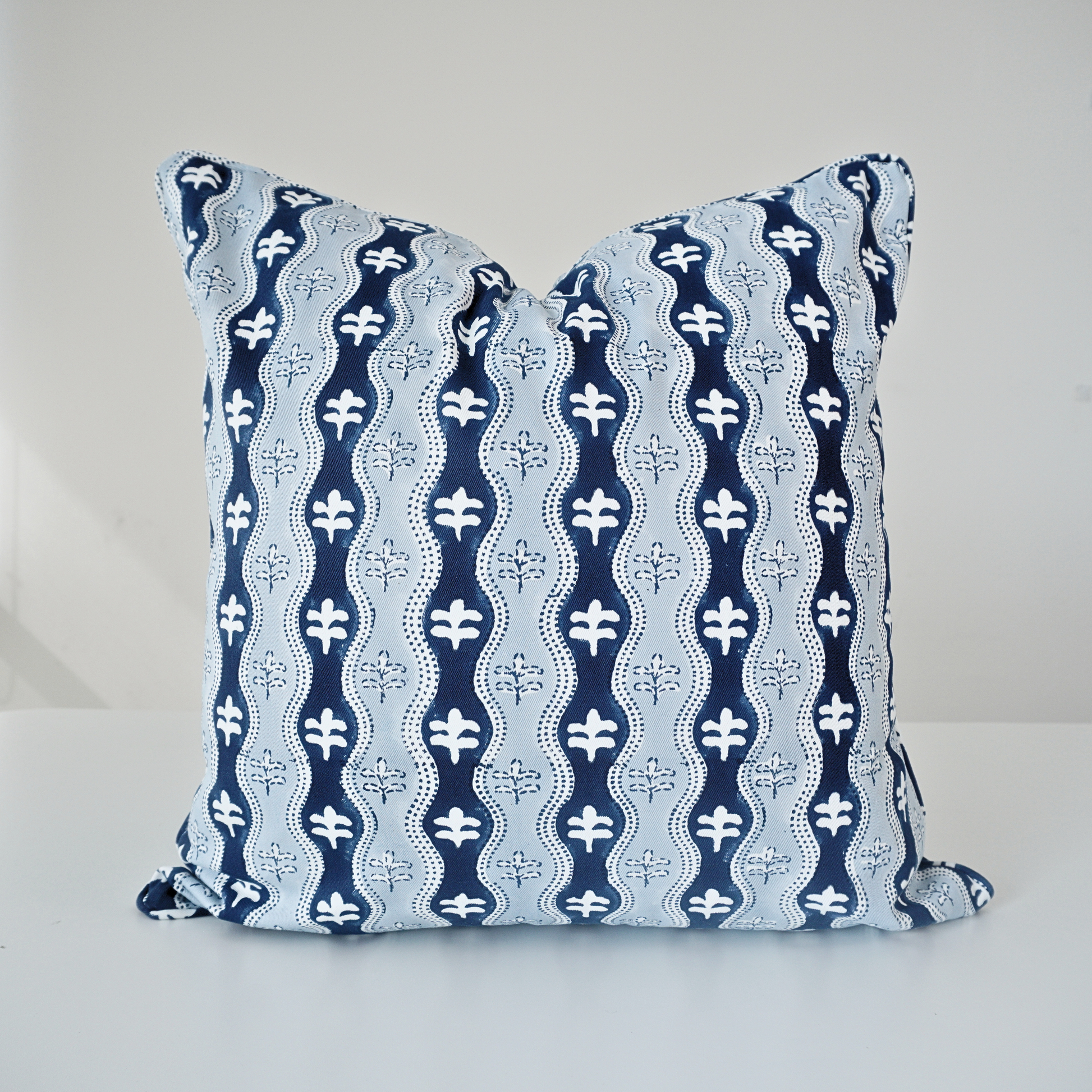 Studio product shot of a single Nami Indigo cushion cover by Homeway Living, centered on a neutral background. Handcrafted from 100% cotton, it features a rich indigo blue and light blue wave pattern detailed with small floral motifs. Finished with tailored piped edges, this block-printed artisan piece offers a clean, high-end look ideal for modern rustic, coastal, or contemporary styling.