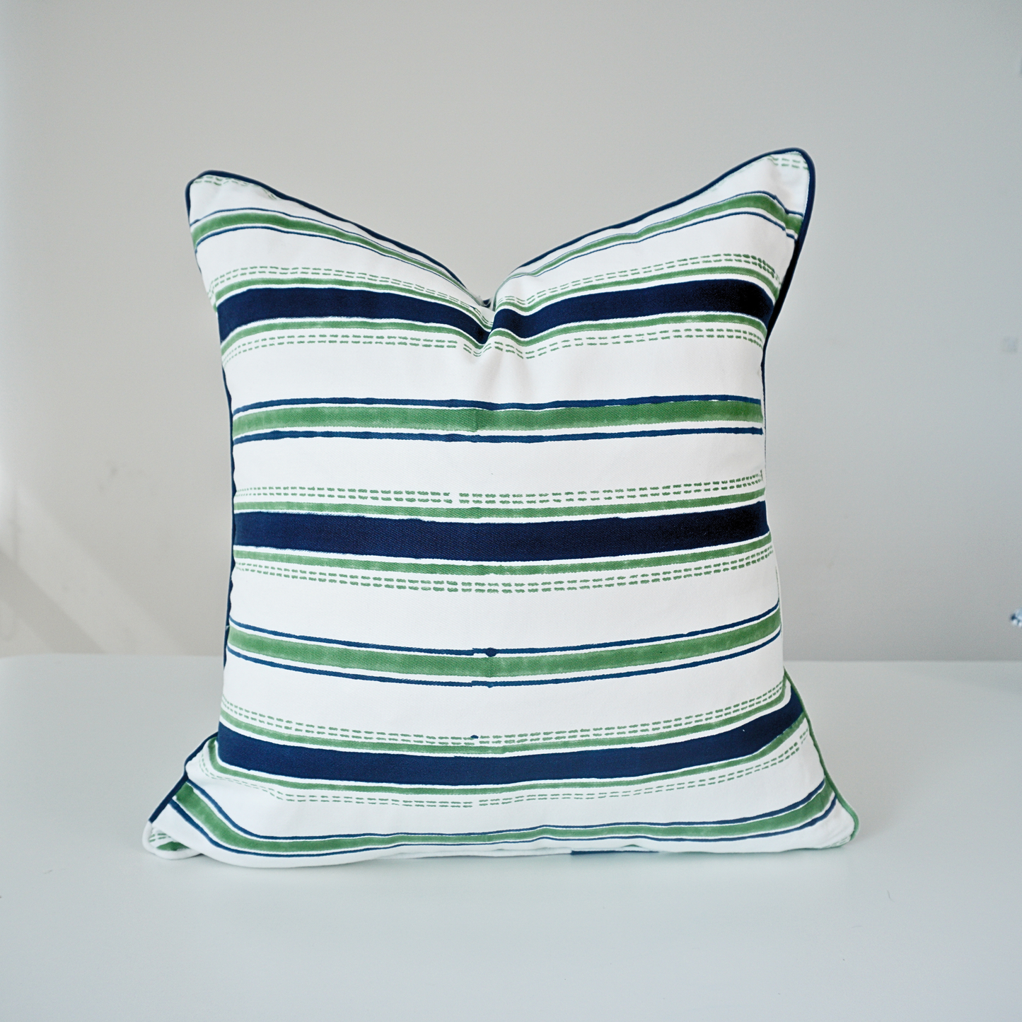 Square Orai Indigo 100% cotton block printed pillow cover. This artisan throw cushion features a classic horizontal stripe pattern in deep indigo blue and fresh green with dashed line details on a crisp white background with piped edges. Fine handmade textile home decor.