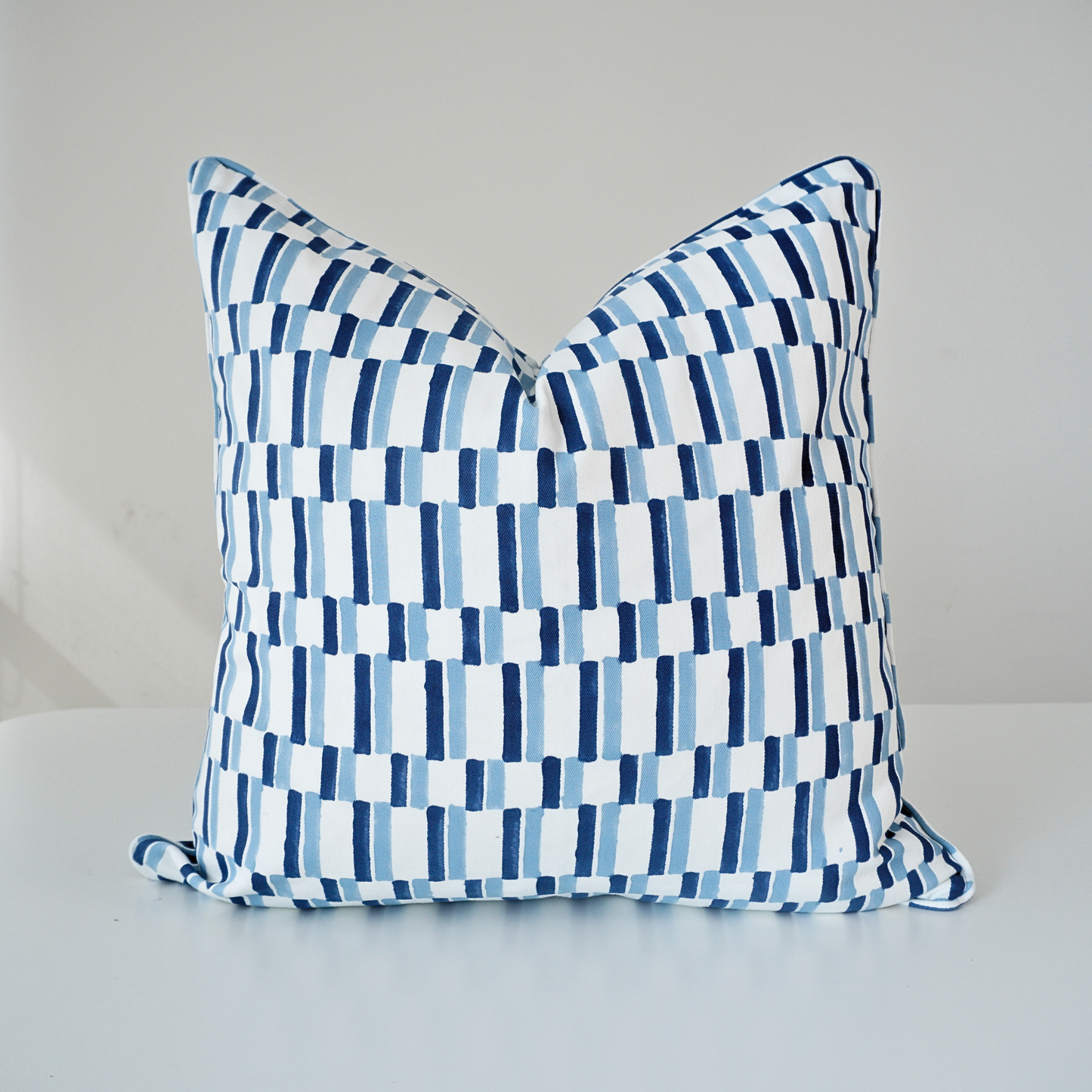 Square Oslo Cerulean 100% cotton block printed pillow cover. This modern throw cushion features a geometric vertical dash grid pattern in shades of cerulean blue and navy on a white background with piped edges. Handmade textile home decor.