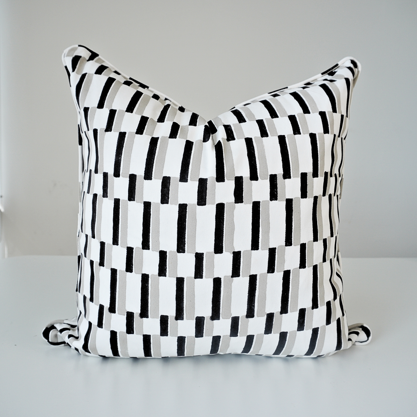A square Oslo Stone 100% cotton block printed pillow cover. This artisan throw cushion showcases a modern geometric pattern of black and light grey vertical rectangular dashes set against a crisp white background. It is finished with tailored piped edges, reflecting a clean, high-end aesthetic in handmade textile home decor.