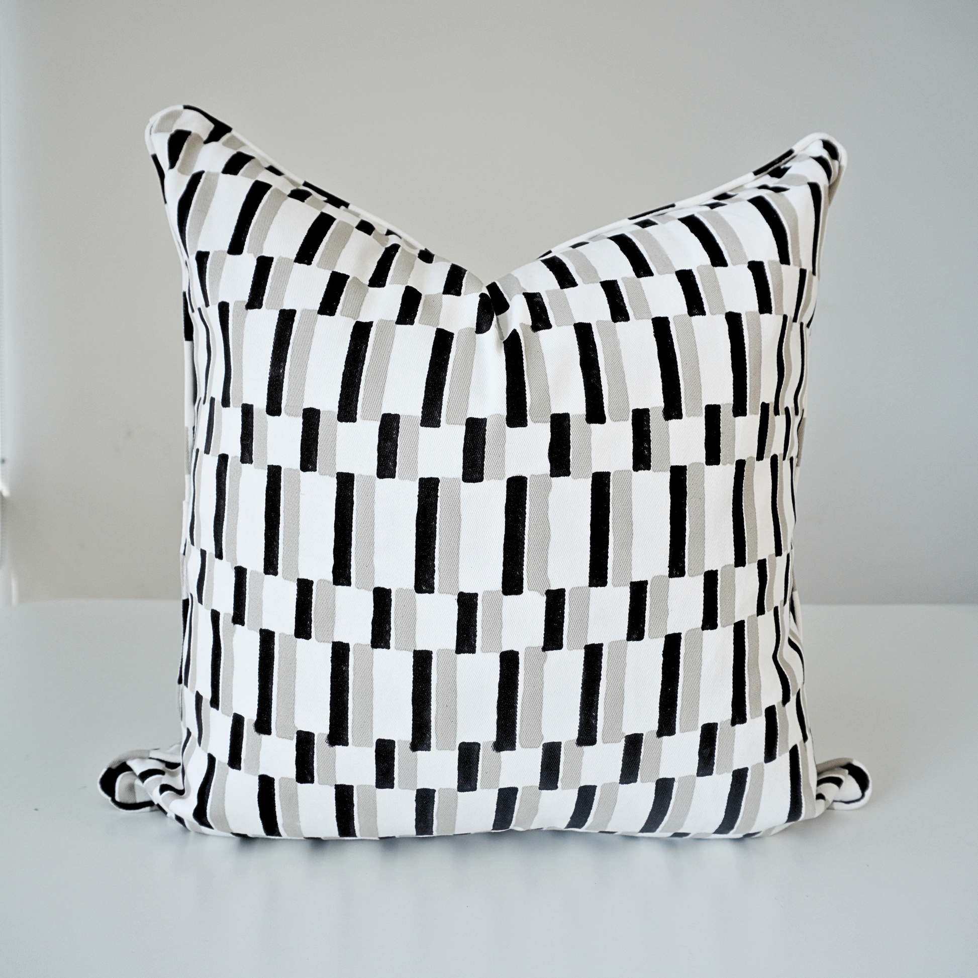 A square Oslo Stone 100% cotton block printed pillow cover. This artisan throw cushion showcases a modern geometric pattern of black and light grey vertical rectangular dashes set against a crisp white background. It is finished with tailored piped edges, reflecting a clean, high-end aesthetic in handmade textile home decor.