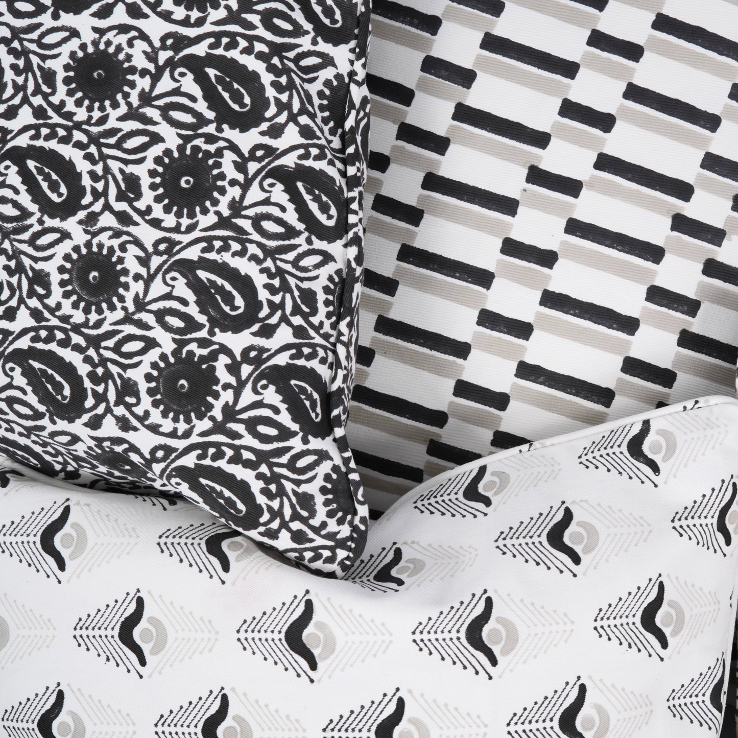 A collection of decorative throw pillows with various geometric patterns. The pillows feature designs in black, white, and gray. Patterns include stripes, dashes, and stylized feather shapes, creating a modern aesthetic.