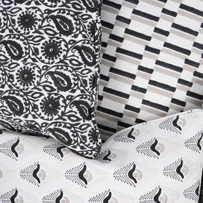 A collection of decorative throw pillows with various geometric patterns. The pillows feature designs in black, white, and gray. Patterns include stripes, dashes, and stylized feather shapes, creating a modern aesthetic.