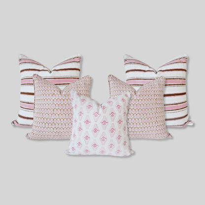 A curated set of five handmade 100% cotton cushion covers arranged in a pyramid on a neutral background. The collection includes two pink and brown striped covers, two with a repeating pink and brown fan-arch pattern, and a central cushion with a pink geometric arrow motif. Each artisanal piece is finished with tailored piped edges, showcasing a clean, high-end aesthetic.