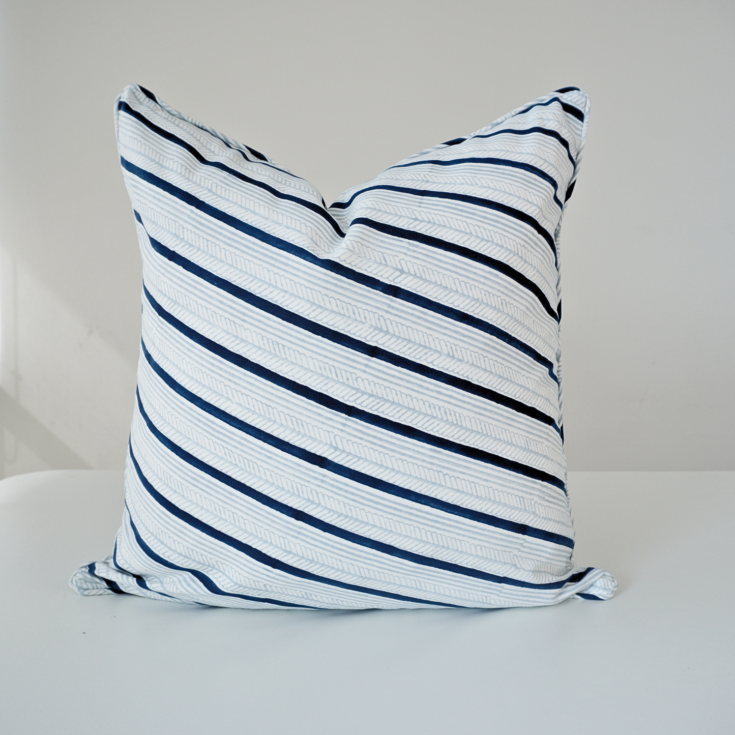 Studio product shot of a single Serere Frost cushion cover by Homeway Living, centered on a neutral background. Handcrafted from 100% cotton, it features diagonal navy blue and light grey stripes with subtle textured line details on a crisp white base. Finished with tailored piped edges, this block-printed artisan piece offers a clean, modern aesthetic perfect for coastal or Scandinavian decor.