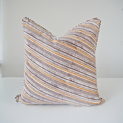 A square throw pillow with a brown, beige, and white hand-drawn patterned design, resting on a white surface against a light gray background.