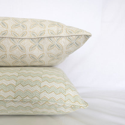 A close-up side view of a stack of two hand-block printed cushions against a crisp white background. The top cushion features the delicate soft blue and tan geometric floral pattern of the Bali plumeria Breeze design, elegantly resting on a coordinating wavy sage green and tan chevron patterned cushion. This detail shot highlights the neatly finished piped edges, showcasing the high quality of these handcrafted textiles that perfectly add a light, cozy modern rustic Canadian farmhouse aesthetic to any home