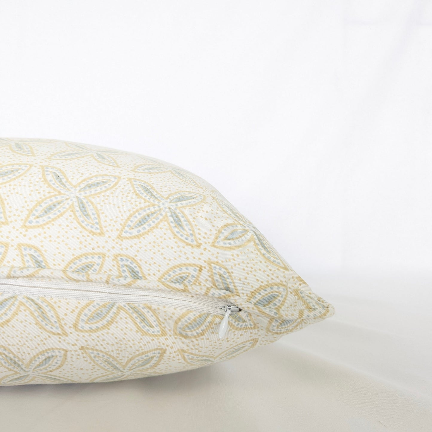 A close-up side view of the hand-block printed Bali plumeria Breeze cushion resting on a crisp white background. This detailed shot highlights the neatly sewn discreet hidden zipper closure. The soft blue and tan floral geometric pattern showcases the quality of this handcrafted textile, perfectly adding a light, cozy modern rustic Canadian farmhouse aesthetic to your home decor.