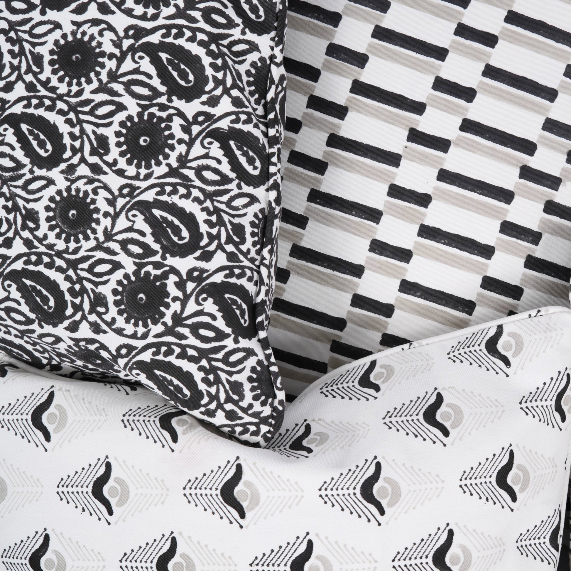 Close-up of three layered 100% cotton block printed pillow covers. Features the Siona Charcoal black and white floral paisley, the Oslo Stone geometric dash pattern, and a coordinating stylized arrow motif cushion in black, grey, and white. Fine handmade artisan home decor showcasing a clean, high-end aesthetic.