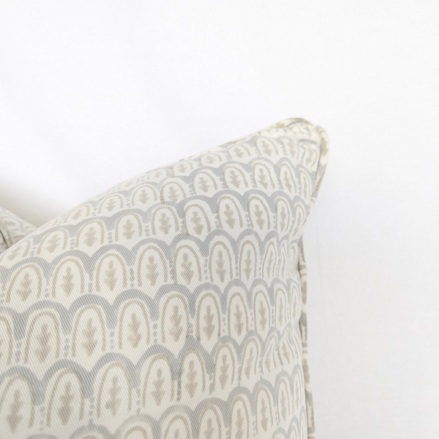 A close-up corner view of a light blue and neutral beige hand-block printed cushion cover, emphasizing the beautifully finished piped edge. The delicate, repeating scalloped arch motif highlights the intricate traditional artisanal craftsmanship involved in creating this textile. This square throw pillow is an ideal accent piece for adding a touch of warm, sophisticated modern rustic farmhouse style to both Canadian and USA interiors.