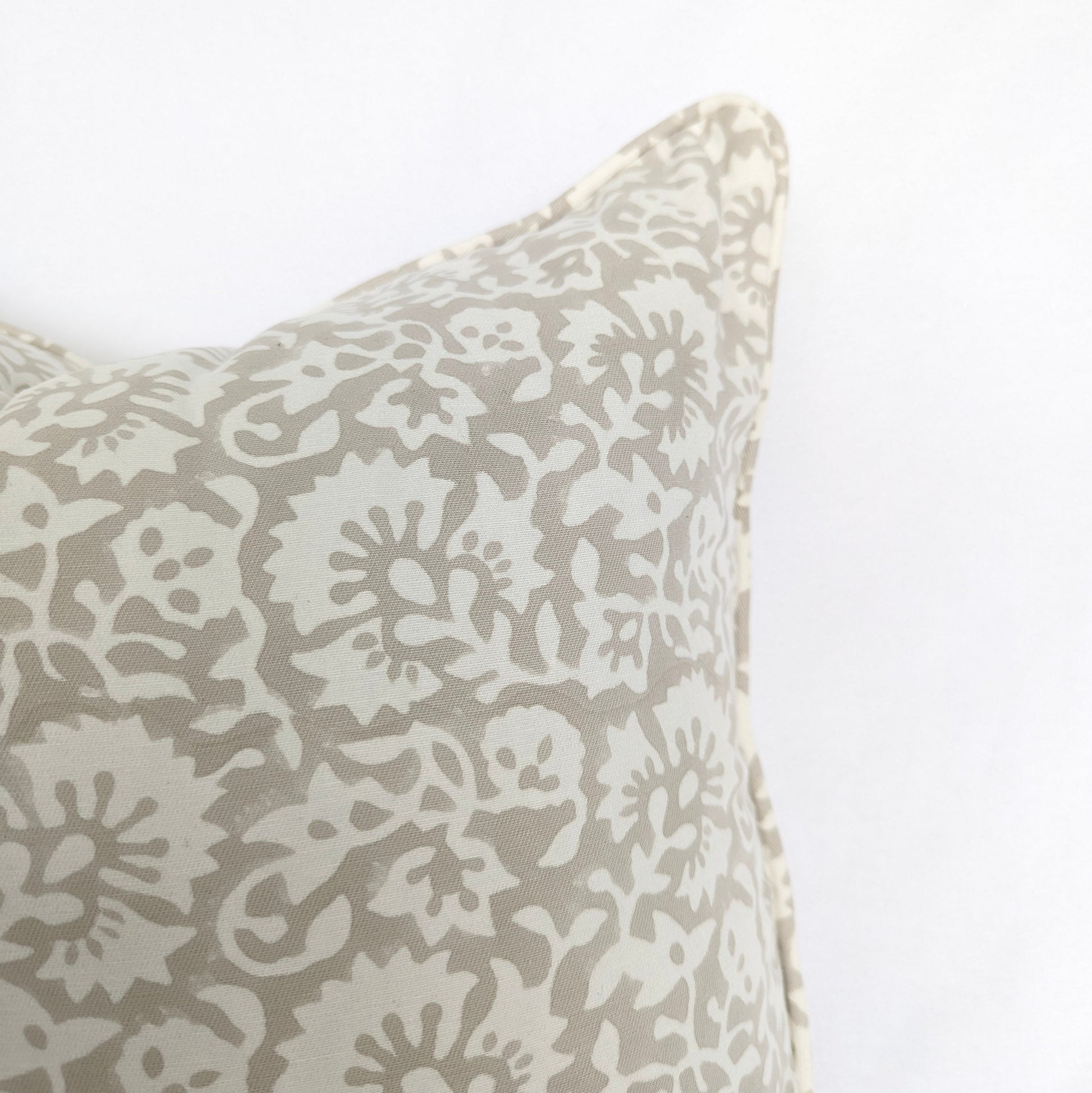A close-up view of the Fiora Muse 100% cotton block printed pillow cover. The image highlights the detailed, dense floral botanical pattern in soft taupe and grey tones on a white background, finished with a tailored piped edge.