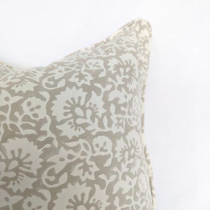 A close-up view of the Fiora Muse 100% cotton block printed pillow cover. The image highlights the detailed, dense floral botanical pattern in soft taupe and grey tones on a white background, finished with a tailored piped edge.
