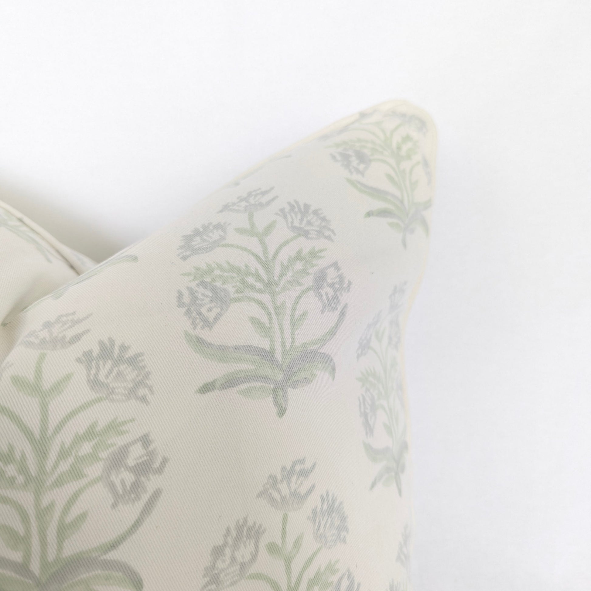 Close-up corner detail of the Jaipuri Breeze 100% cotton block printed pillow and cushion cover against a white background. Highlights the soft sage green repeating floral stem motif on off-white fabric with tailored piped edges. Fine handmade artisan textile home decor.