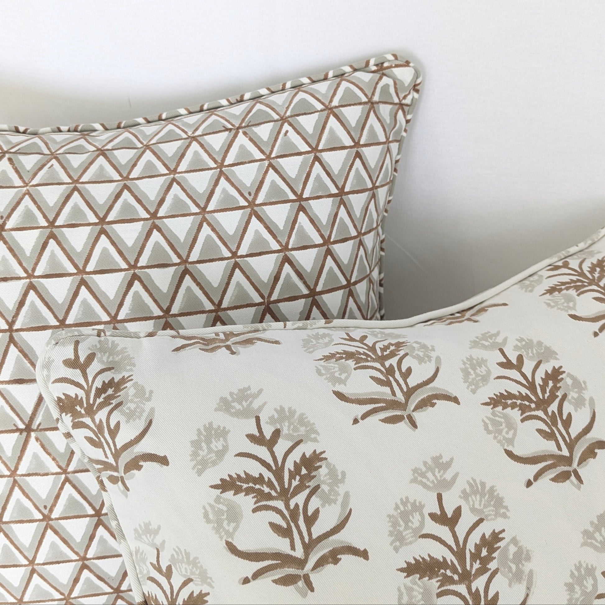 A close-up of two hand-block printed cushion covers. The front pillow highlights an earthy brown floral sprig pattern beautifully layered against a fine geometric triangle design. With piped edges, these artisanal textiles add a cozy modern rustic farmhouse aesthetic for both Canadian and USA homes.