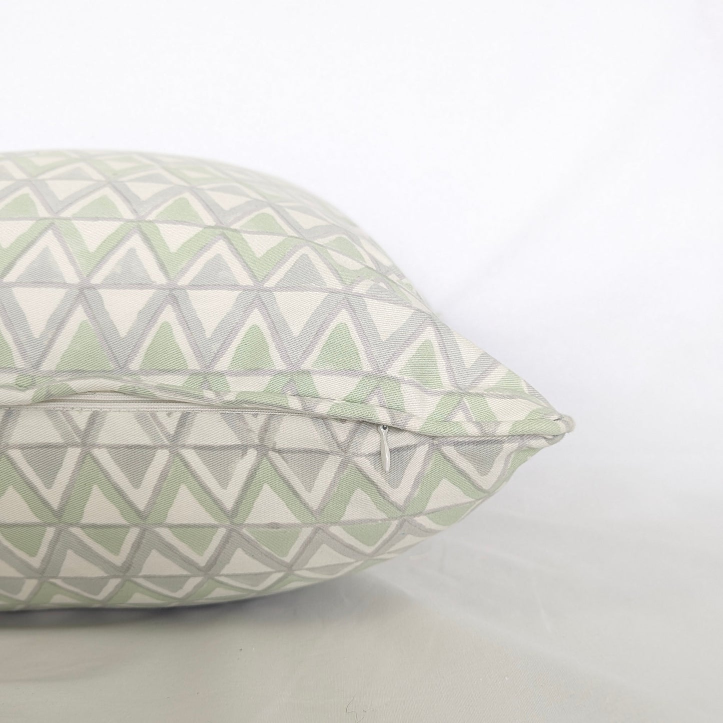 Close-up side view showing the hidden zipper closure and piped seam of the Moroccan Meadow Mist 100% cotton block printed pillow and cushion cover. Features a repeating geometric interlocking triangle pattern in soft meadow green and light grey on white fabric against a clean white background. Fine handmade artisan textile home decor.