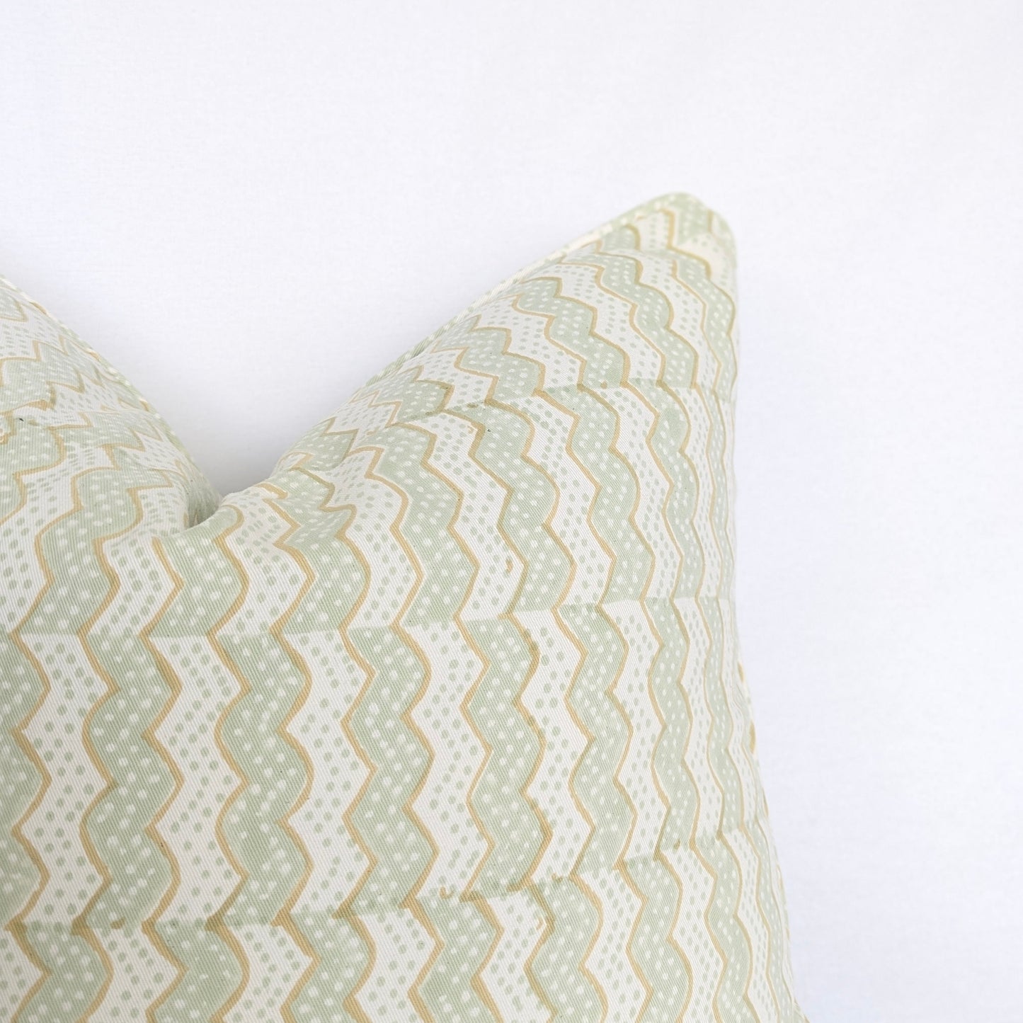 A close-up corner view of the hand-block printed Myra Meadow mist cushion against a crisp white background. This detail highlights the wavy sage green and tan chevron pattern and neatly finished edges. This beautifully handcrafted textile perfectly adds a light, cozy modern rustic Canadian farmhouse aesthetic to your home decor.