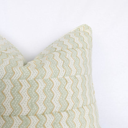 A close-up corner view of the hand-block printed Myra Meadow mist cushion against a crisp white background. This detail highlights the wavy sage green and tan chevron pattern and neatly finished edges. This beautifully handcrafted textile perfectly adds a light, cozy modern rustic Canadian farmhouse aesthetic to your home decor.