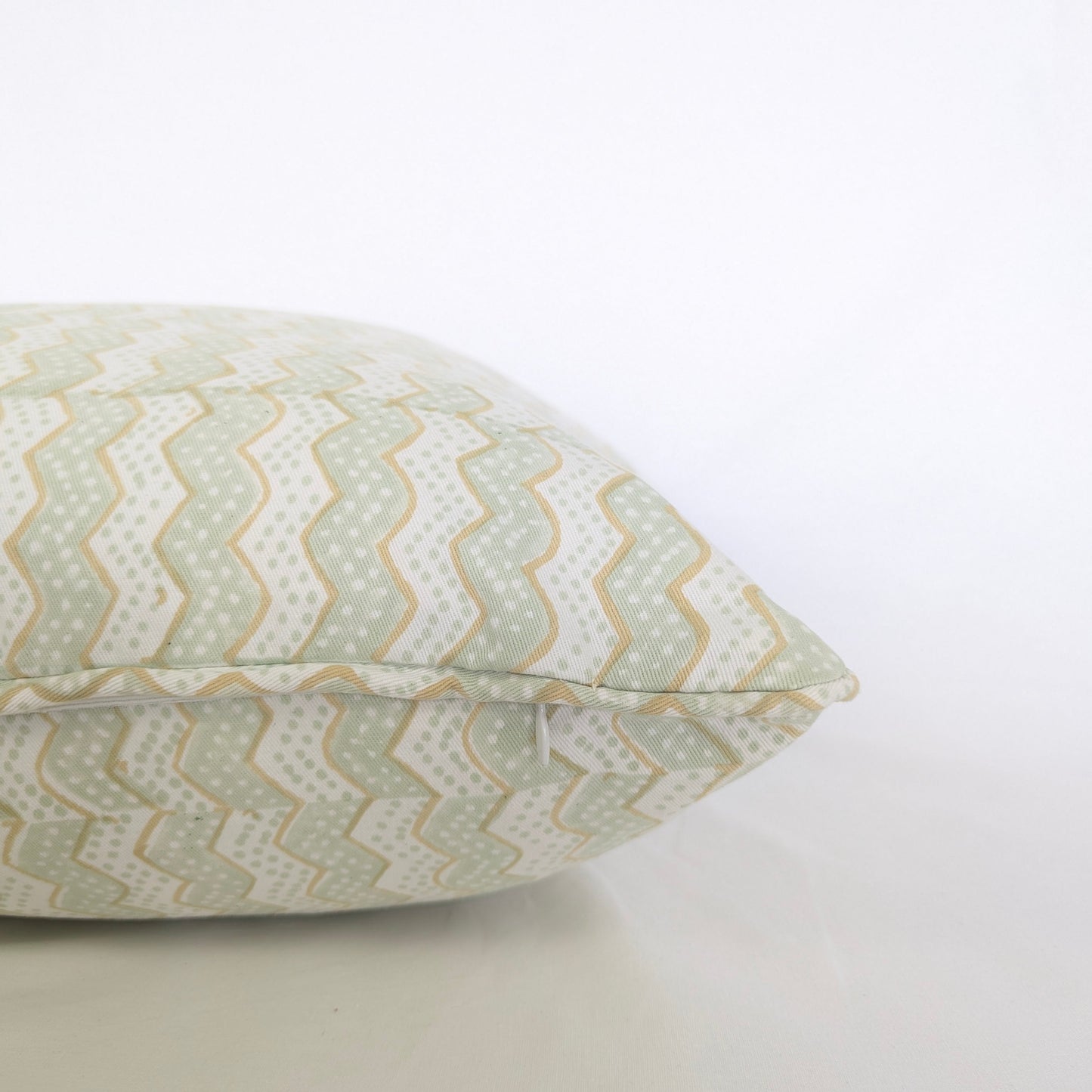 A close-up side view of the hand-block printed Myra Meadow mist cushion on a crisp white background. This detailed shot highlights the neatly sewn discreet hidden zipper closure and piped edges. The wavy sage green and tan chevron pattern showcases the quality of this handcrafted textile, perfectly adding a light, cozy modern rustic Canadian farmhouse aesthetic to your home decor.