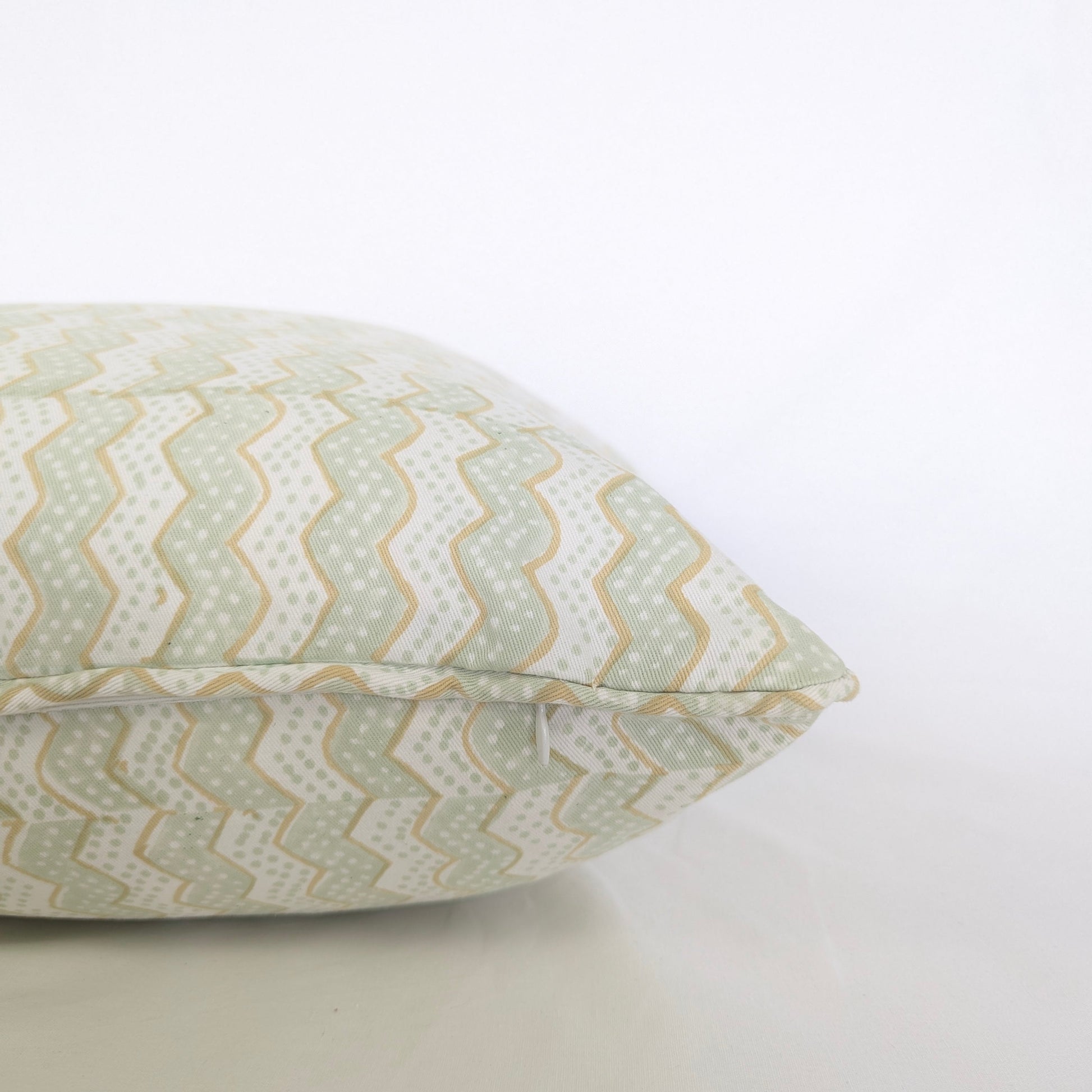 A close-up side view of the hand-block printed Myra Meadow mist cushion on a crisp white background. This detailed shot highlights the neatly sewn discreet hidden zipper closure and piped edges. The wavy sage green and tan chevron pattern showcases the quality of this handcrafted textile, perfectly adding a light, cozy modern rustic Canadian farmhouse aesthetic to your home decor.