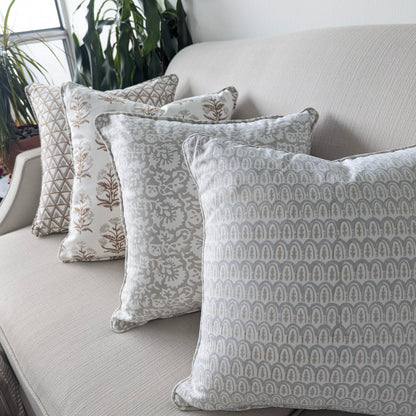 A beautiful arrangement of four hand-block printed cushions lined up on a neutral textured sofa. The coordinating collection features soft grey and earthy tan tones, showcasing a mix of geometric scalloped arches, elegant botanical florals, and triangle patterns. These elegantly handcrafted textiles perfectly add a cozy modern rustic Canadian farmhouse aesthetic to your living room decor.