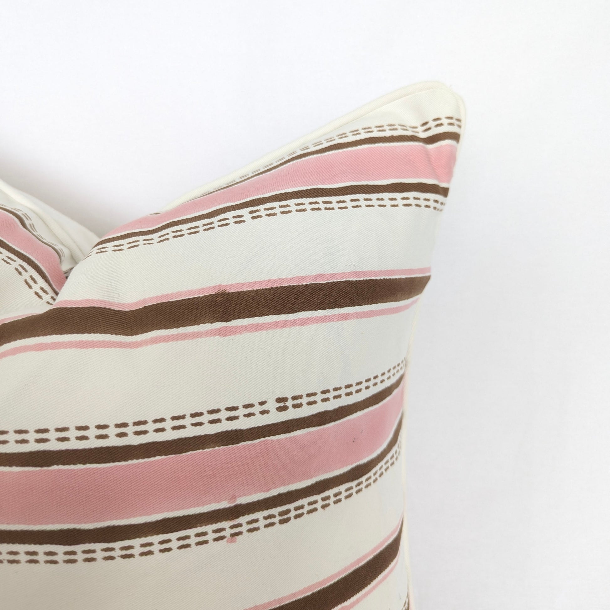 A close-up corner view of the hand-block printed Orai Soil cushion on a white background. This detailed shot highlights the tailored piped edges and the horizontal pattern of soft pink bands alternating with solid and dashed earthy brown stripes. This handcrafted textile adds a cozy modern rustic Canadian farmhouse aesthetic to your home decor.