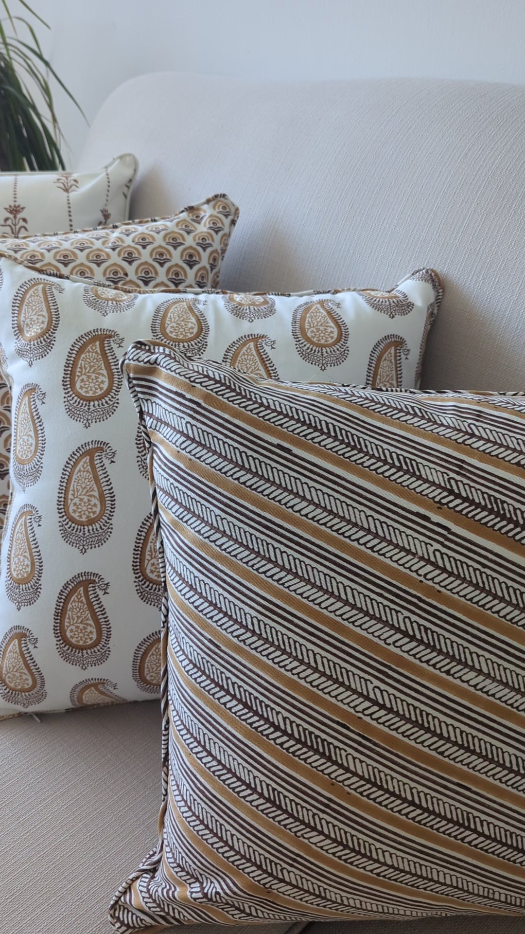 A short video showcasing a beautifully curated arrangement of hand-block printed cushions lined up on a neutral textured sofa. The coordinating collection features warm ochre and earthy brown tones, highlighting a mix of diagonal stripes, classic paisley, and geometric arch patterns. These elegantly handcrafted textiles perfectly add a cozy modern rustic Canadian farmhouse aesthetic to your living room decor.