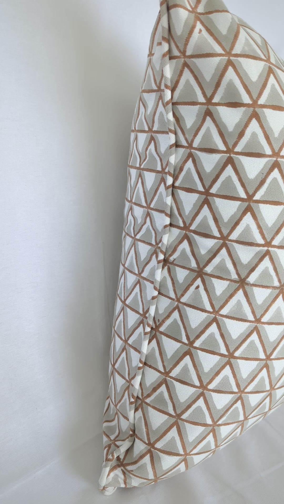 A short video showcasing a close-up of a hand-block printed cushion featuring an earthy tan and soft grey geometric triangle pattern on a cream background. Highlighting the side profile and piped edge, this beautifully handcrafted textile perfectly adds a cozy modern rustic Canadian farmhouse aesthetic to your home decor.