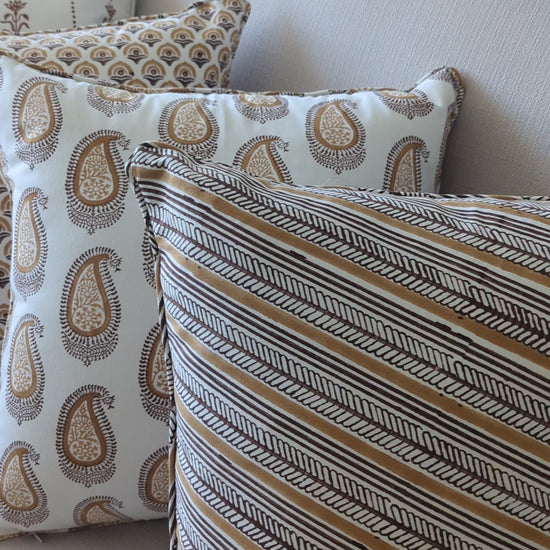 A short video showcasing a collection of hand-block printed cushions on a neutral sofa. The foreground features a diagonal brown and ochre striped cushion, elegantly layered with a matching warm ochre paisley pattern. These earthy, handcrafted textiles perfectly add a cozy modern rustic Canadian farmhouse aesthetic to your living room decor.