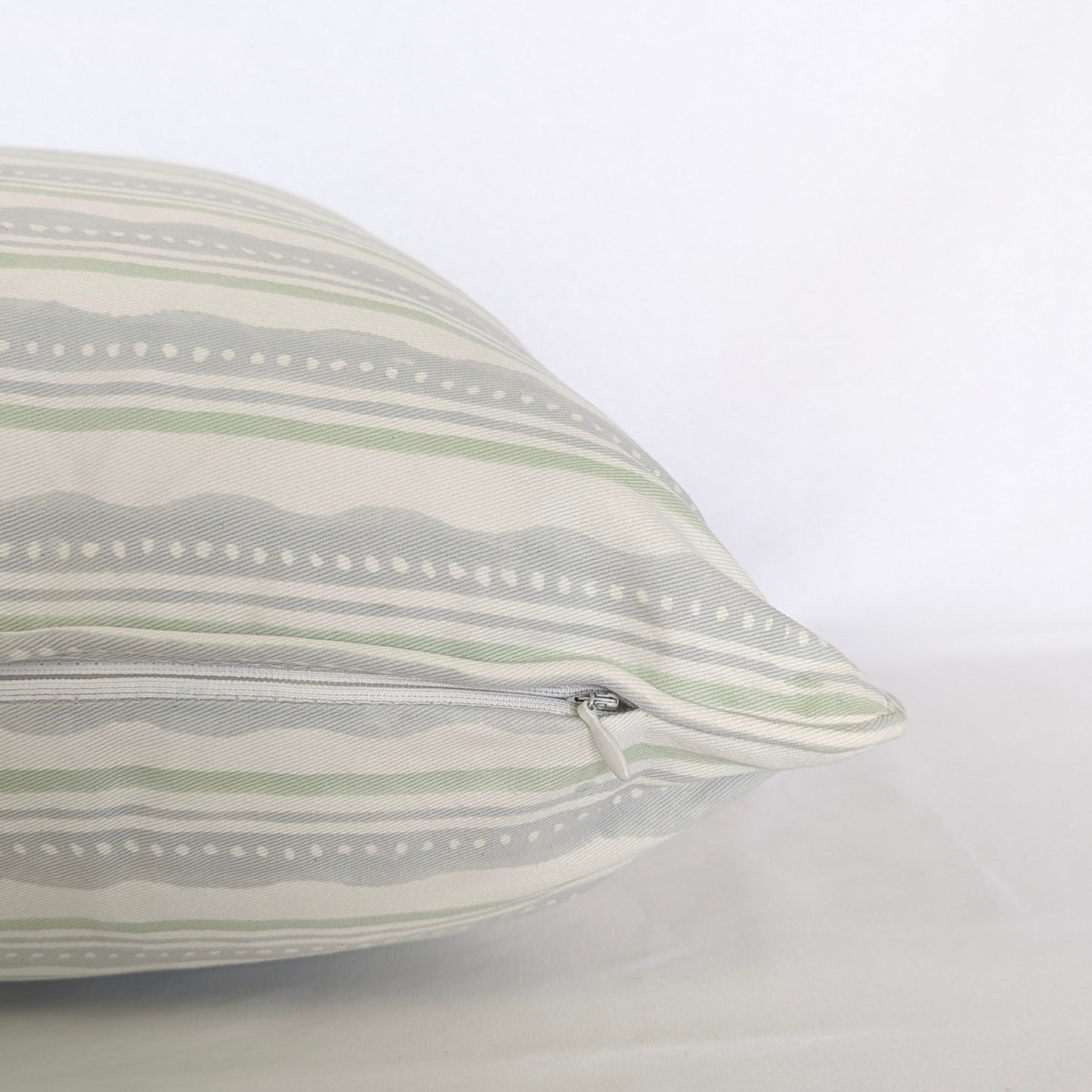 A close-up side view of the "Amalfi Breeze" hand-block printed cushion, showcasing its refreshing sage green and light blue horizontal striped and wavy pattern on a crisp white background. This detail shot highlights the neatly sewn, discreet hidden zipper closure, emphasizing the quality of this handcrafted textile that perfectly adds a cozy modern rustic Canadian farmhouse aesthetic to any home decor.