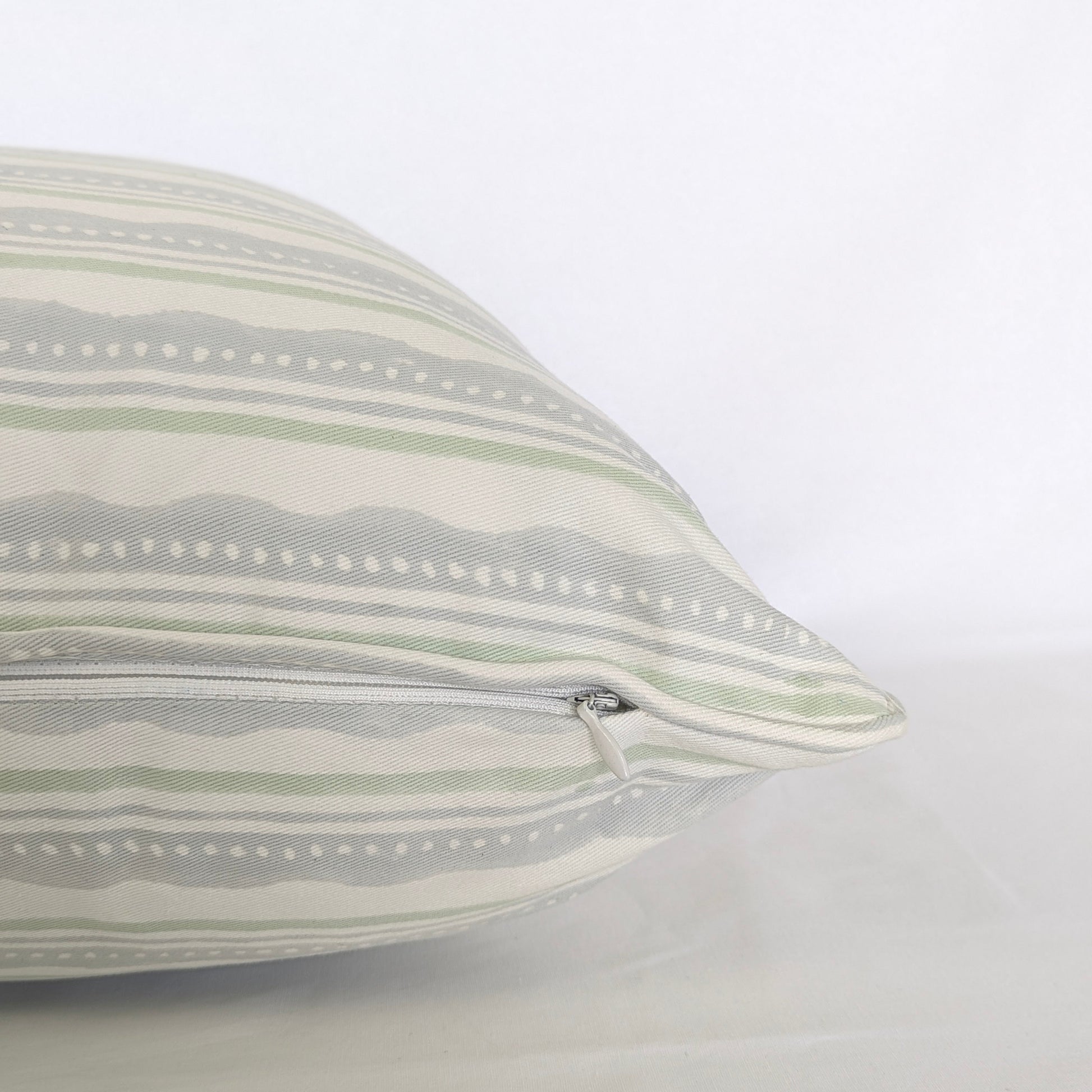 A close-up side view of the "Amalfi Breeze" hand-block printed cushion, showcasing its refreshing sage green and light blue horizontal striped and wavy pattern on a crisp white background. This detail shot highlights the neatly sewn, discreet hidden zipper closure, emphasizing the quality of this handcrafted textile that perfectly adds a cozy modern rustic Canadian farmhouse aesthetic to any home decor.