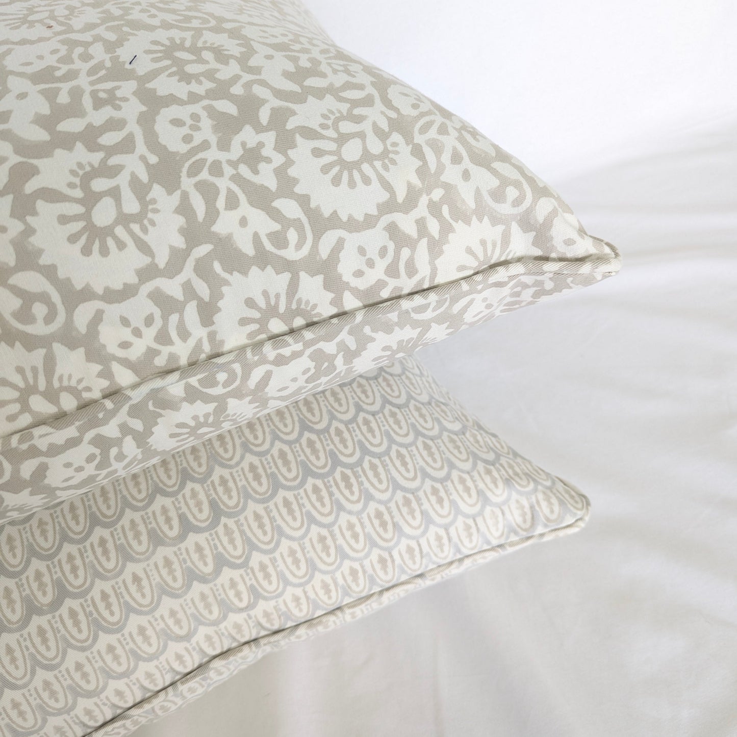 A close-up corner view of two stacked hand-block printed cushion covers. The top pillow features a delicate beige floral motif, resting beautifully above a pale blue and neutral beige scalloped arch pattern. Highlighting artisanal piped edges, this bundle adds a cozy, modern rustic farmhouse aesthetic to both Canadian and USA homes.