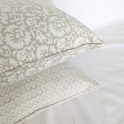 A close-up corner view of two stacked hand-block printed cushion covers. The top pillow features a delicate beige floral motif, resting beautifully above a pale blue and neutral beige scalloped arch pattern. Highlighting artisanal piped edges, this bundle adds a cozy, modern rustic farmhouse aesthetic to both Canadian and USA homes.