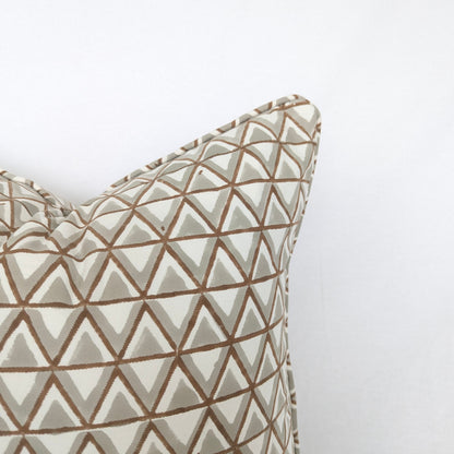 A close-up view of the top corner of a hand-block printed cushion featuring an earthy tan and soft grey geometric triangle pattern on a cream background. This detail shot highlights the neatly finished piped edge, showcasing the quality of this handcrafted textile that perfectly adds a cozy modern rustic Canadian farmhouse aesthetic to any home decor.
